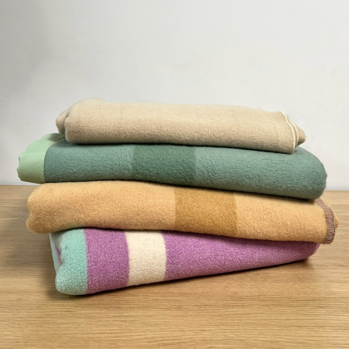 Stack of folded vintage wool camp blankets in various colors on a wooden surface with a light gray background