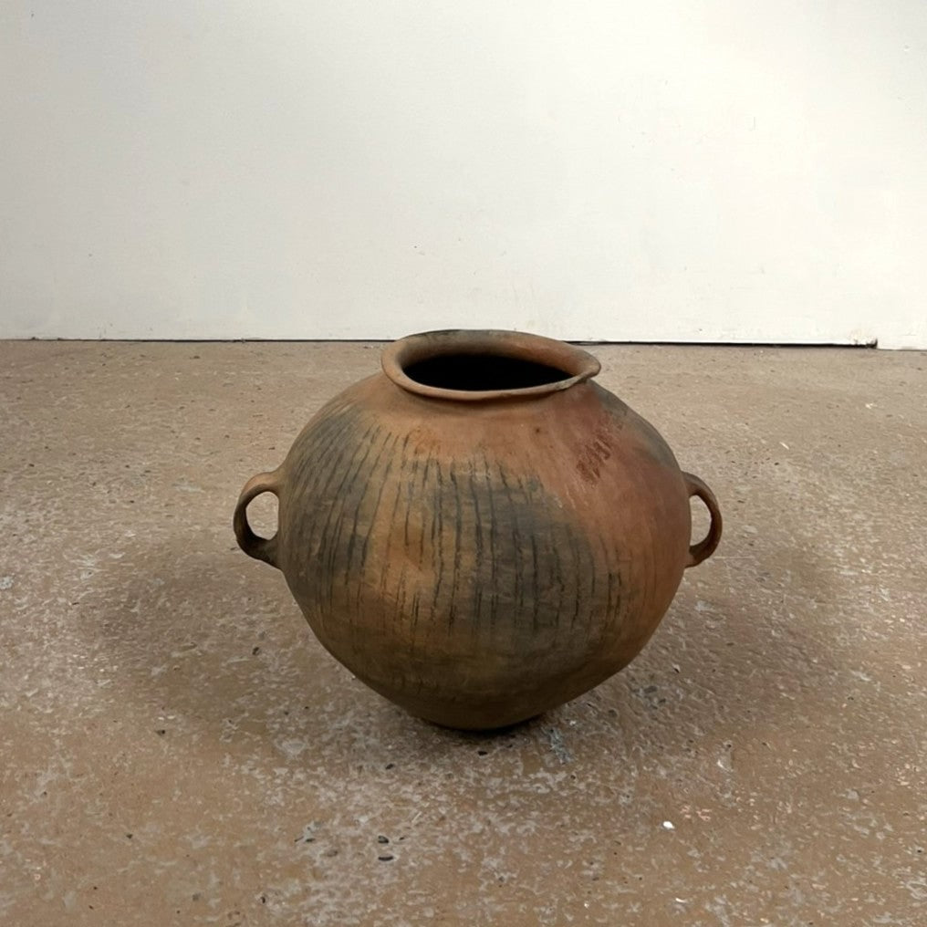 Vintage terracotta pot with handles on a concrete floor.