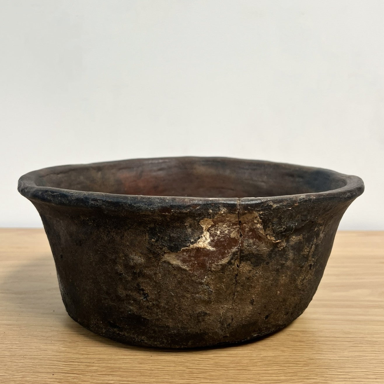 Vintage dark brown ceramic bowl on a light wooden surface with a white background