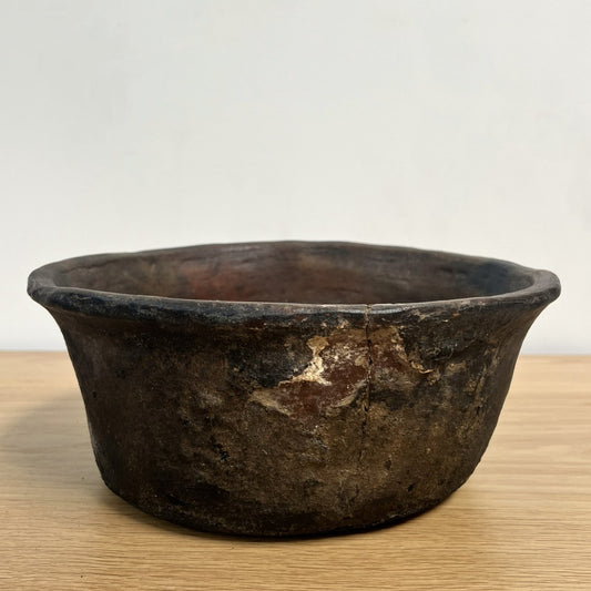 Vintage dark brown ceramic bowl on a light wooden surface with a white background