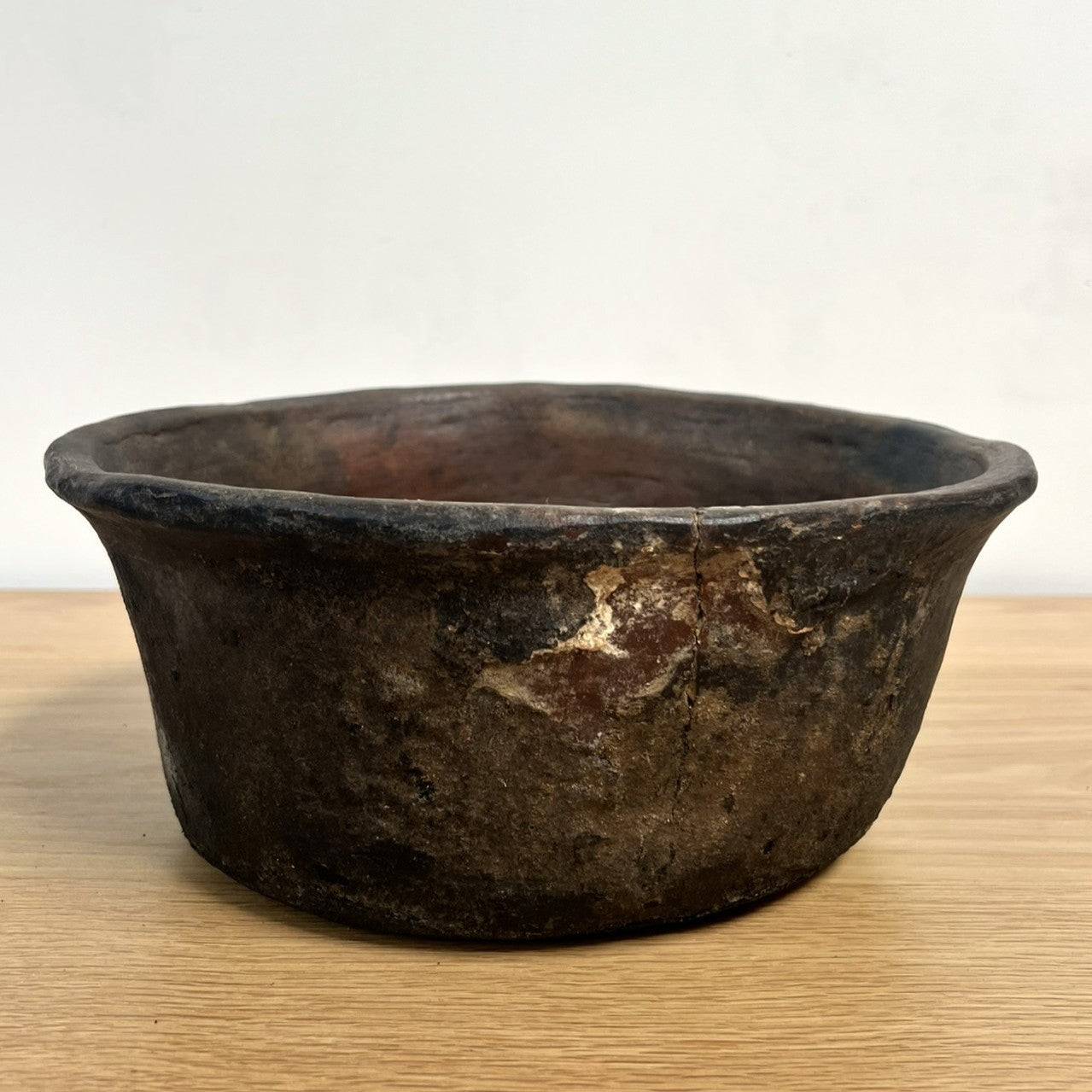 Vintage dark brown ceramic bowl on a light wooden surface with a white background