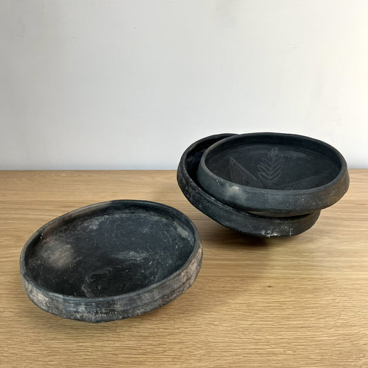 Three black ceramic bowls on a wooden surface with a white background