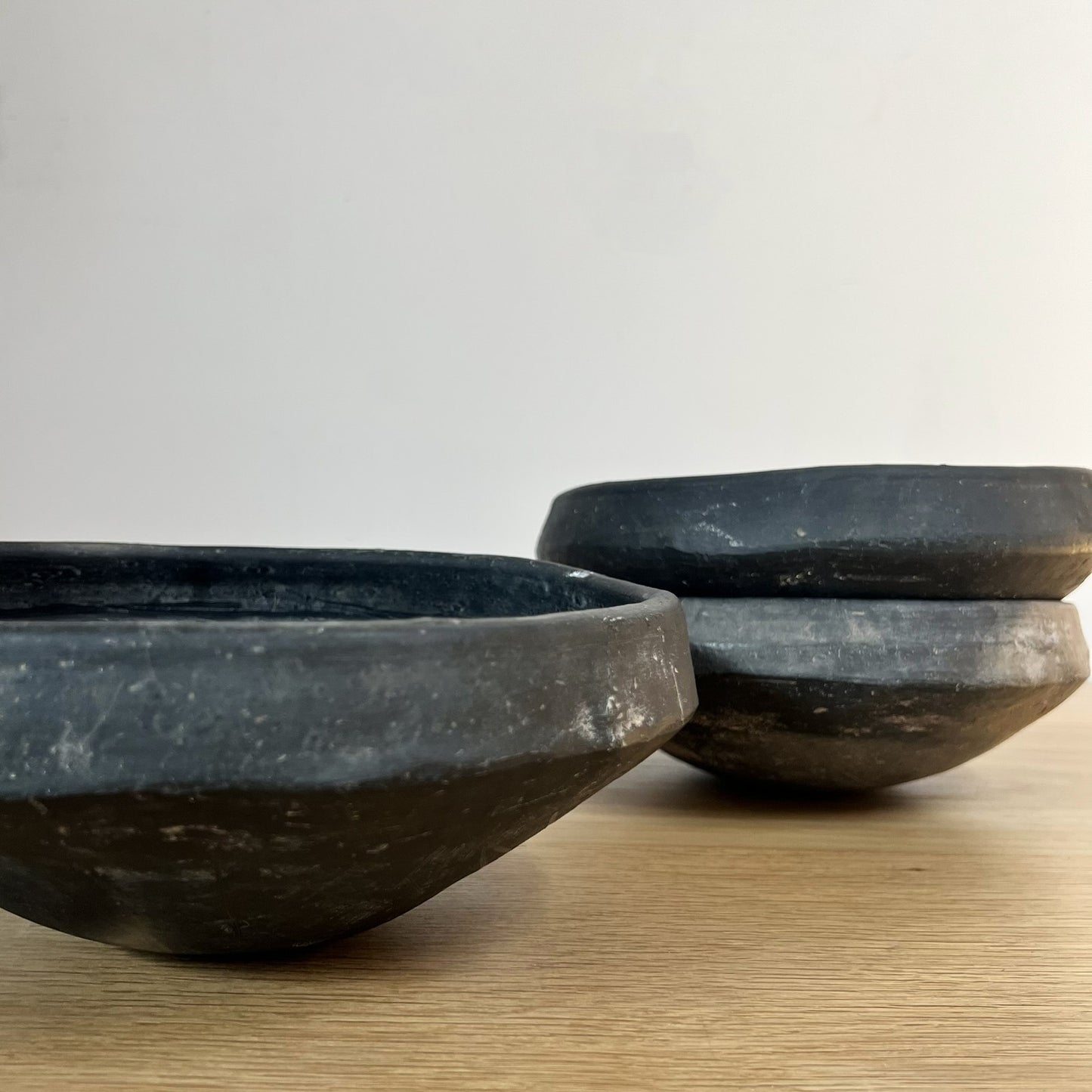Three black stone bowls on a wooden surface with a light gray background