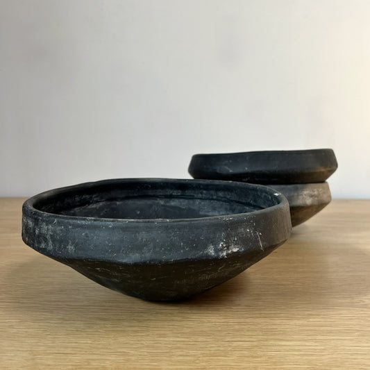 Three black ceramic bowls on a wooden surface with a plain background