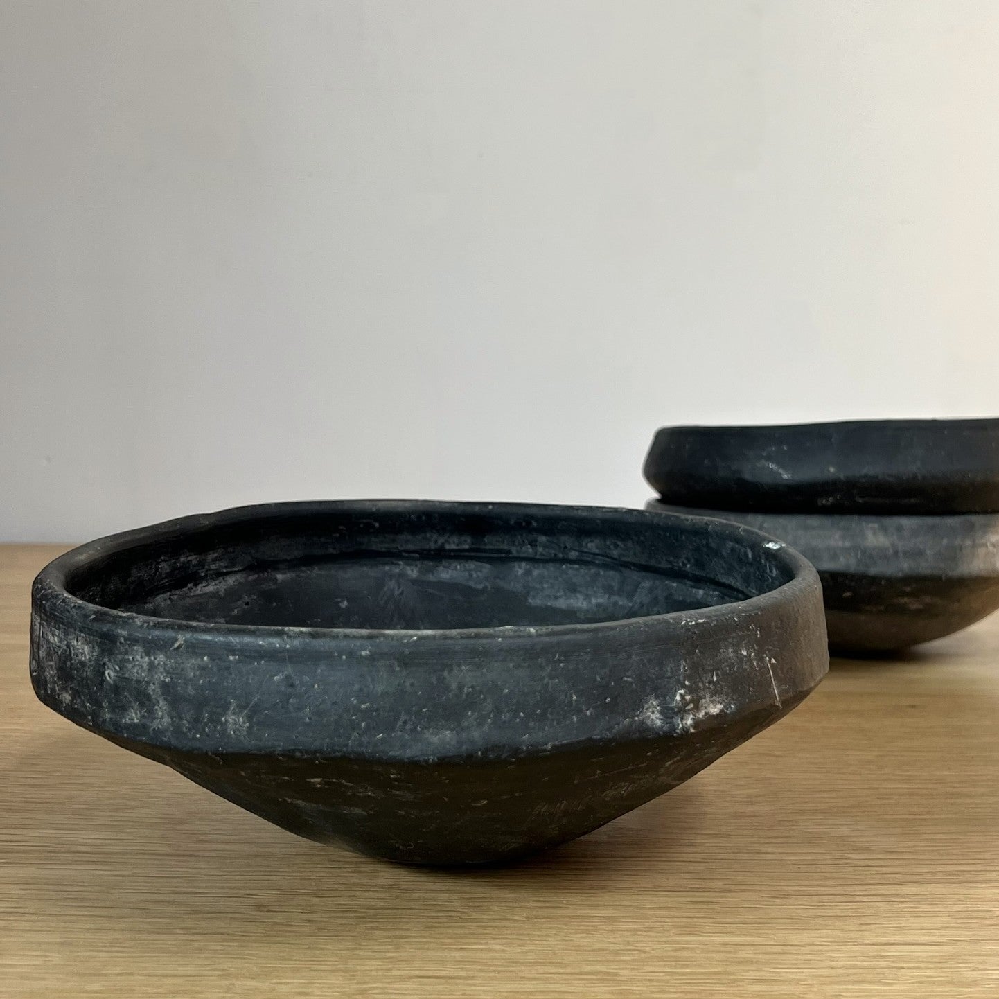 Three black ceramic bowls on a wooden surface with a plain background