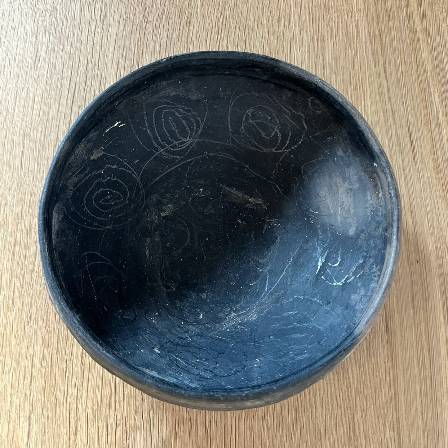 Black ceramic bowl with engraved patterns on a wooden surface