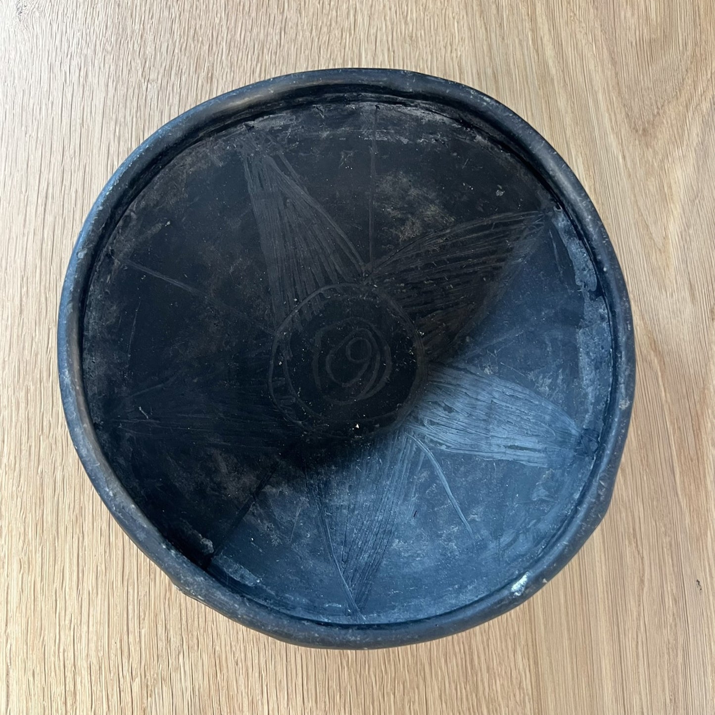 Black ceramic bowl with engraved design on a wooden surface