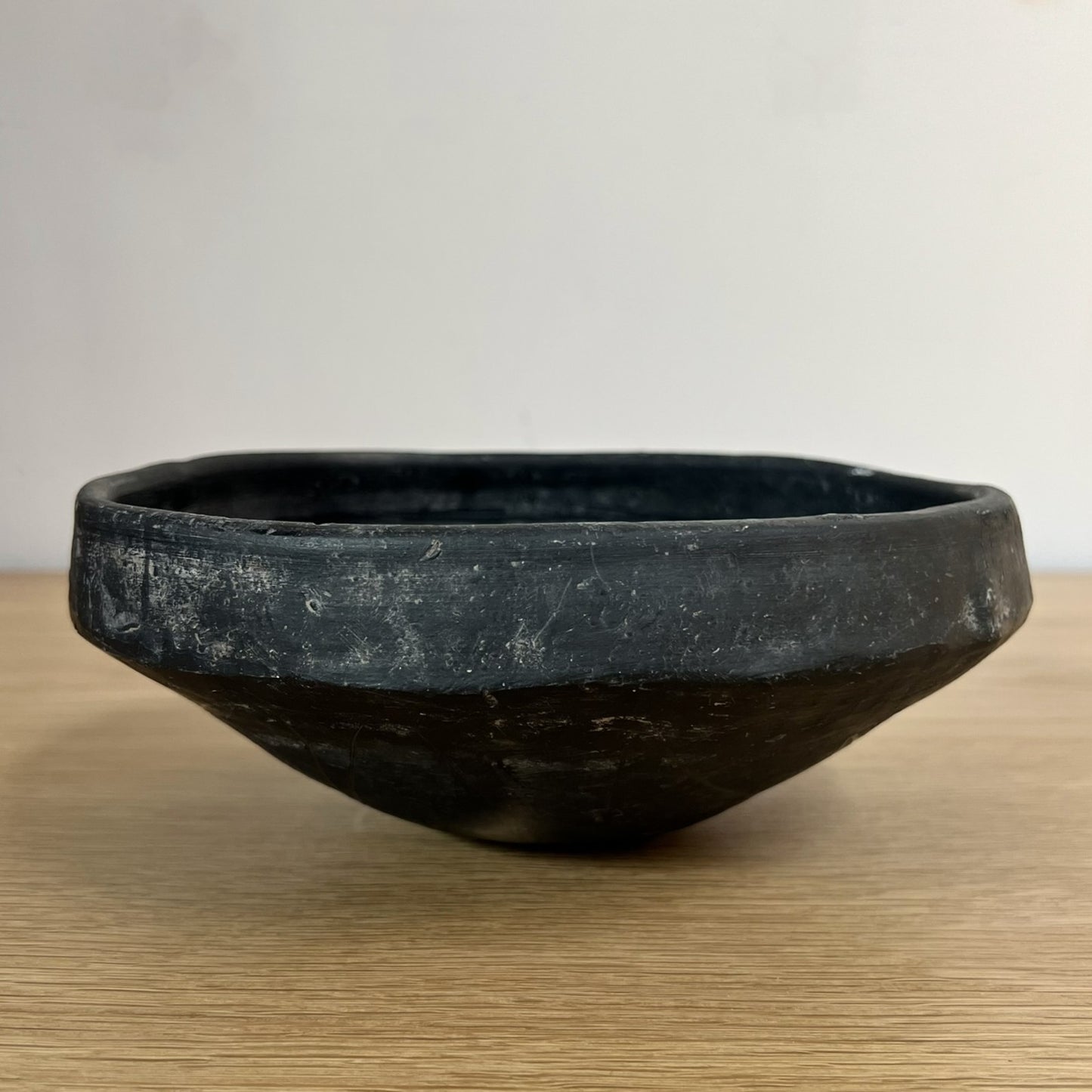 Black ceramic bowl on a wooden surface with a plain background
