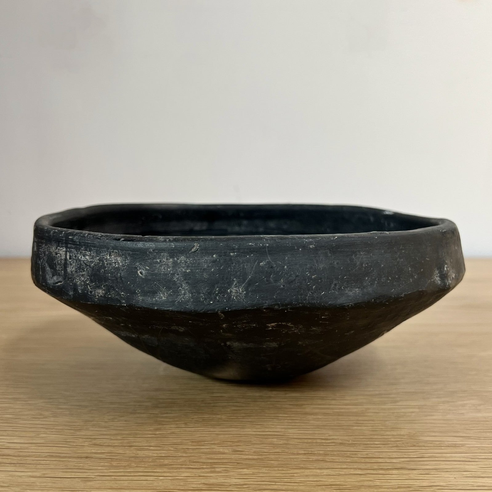 Black ceramic bowl on a wooden surface with a plain background