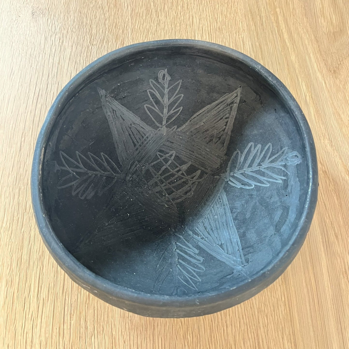 Black ceramic bowl with leaf patterns on a wooden surface